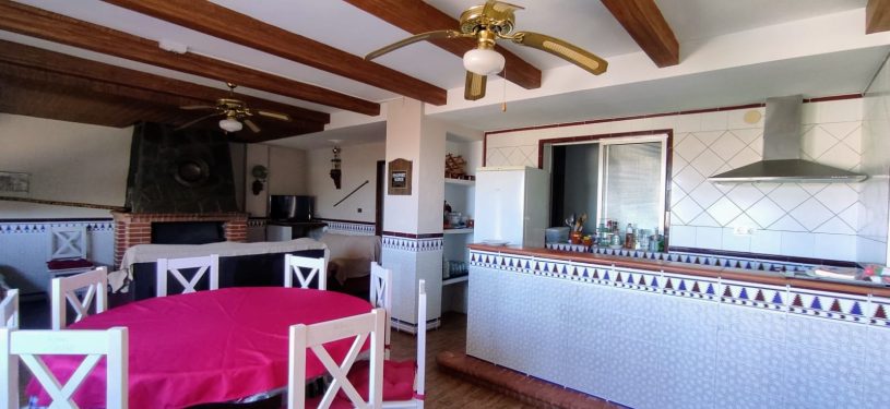 Mesa redonda con sillas de madera y ventanales al fondo. Cocina abierta.